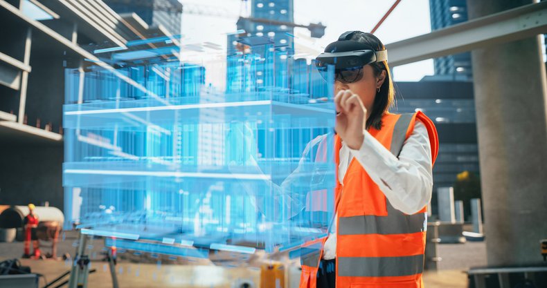 Eine Frau befindet sich auf einer BAustelle. Sie hat eine VR-Brille auf und sieht sich virtuell den geplanten Fortschritt des neuen Gebäudes an.