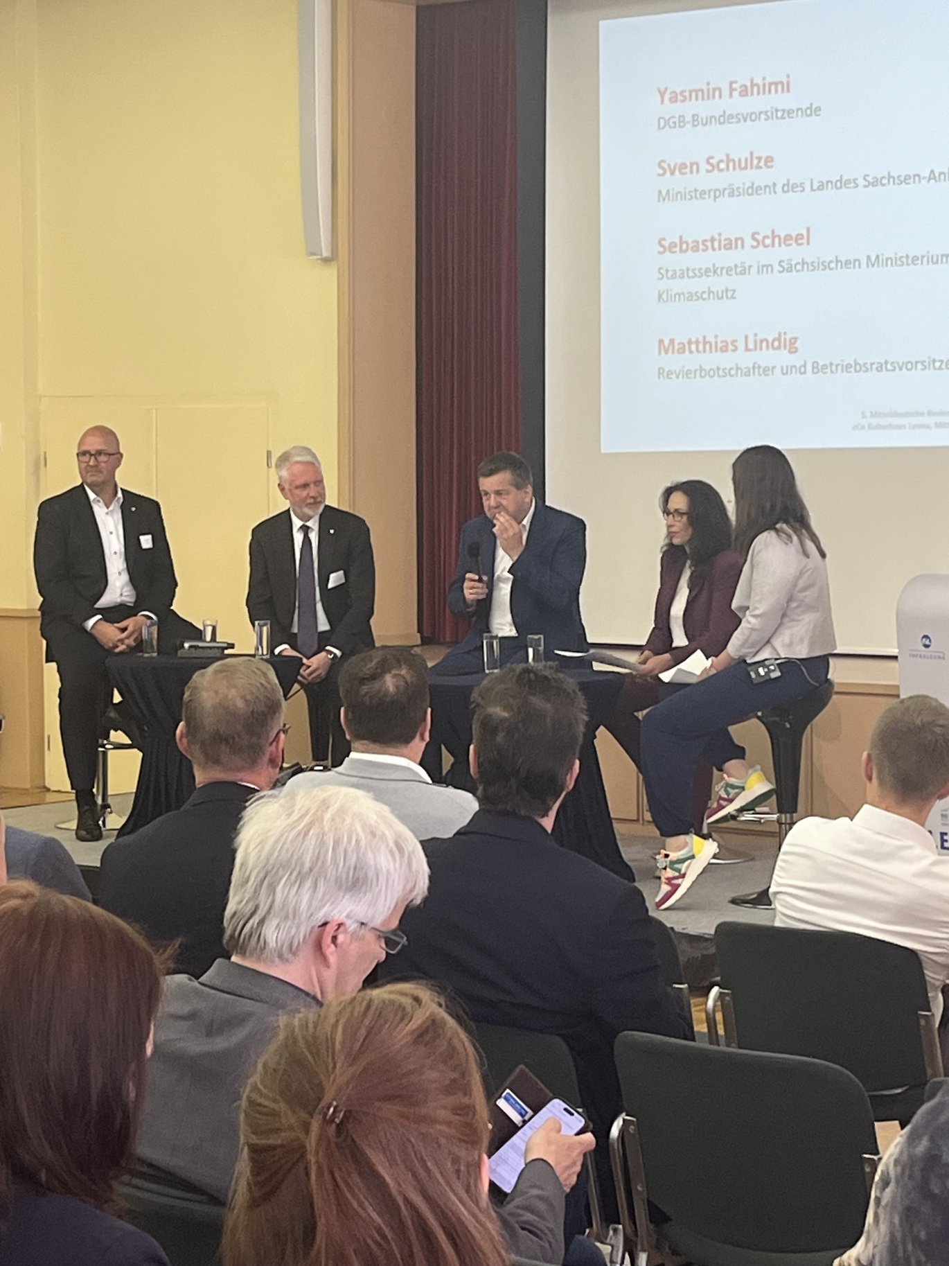 Podiumasdiskussion mit 5 Menschen auf Stüheln auf einer Bühne.