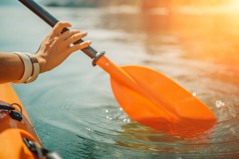 Eine weibliche Hand hält das Paddel eines Kanus und sticht ins Wasser ein